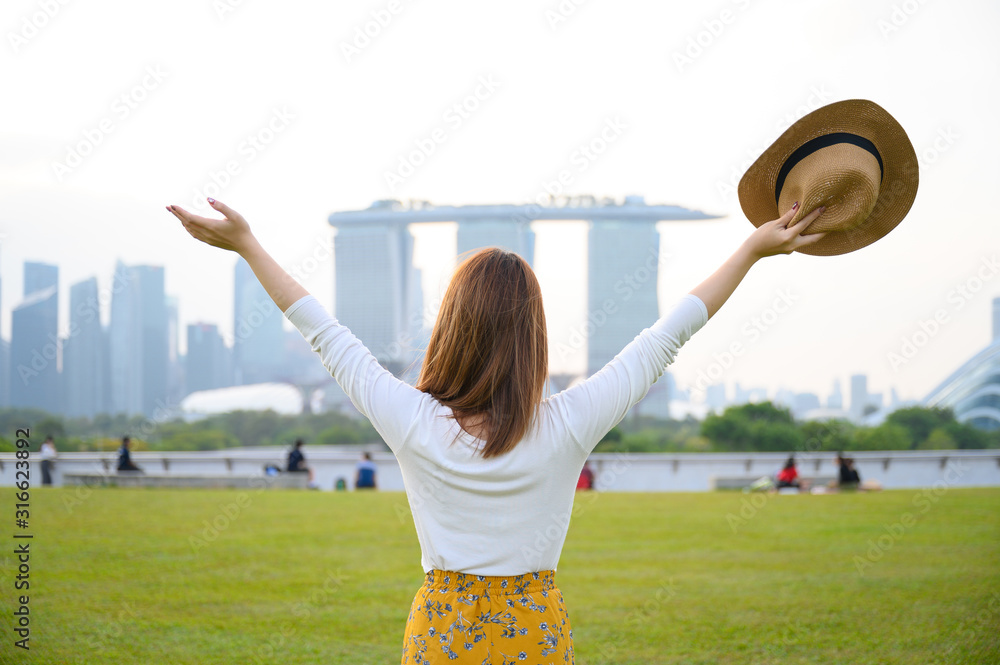 年轻的亚洲女人幸福地站在滨海公园，背景是度假的滨海湾