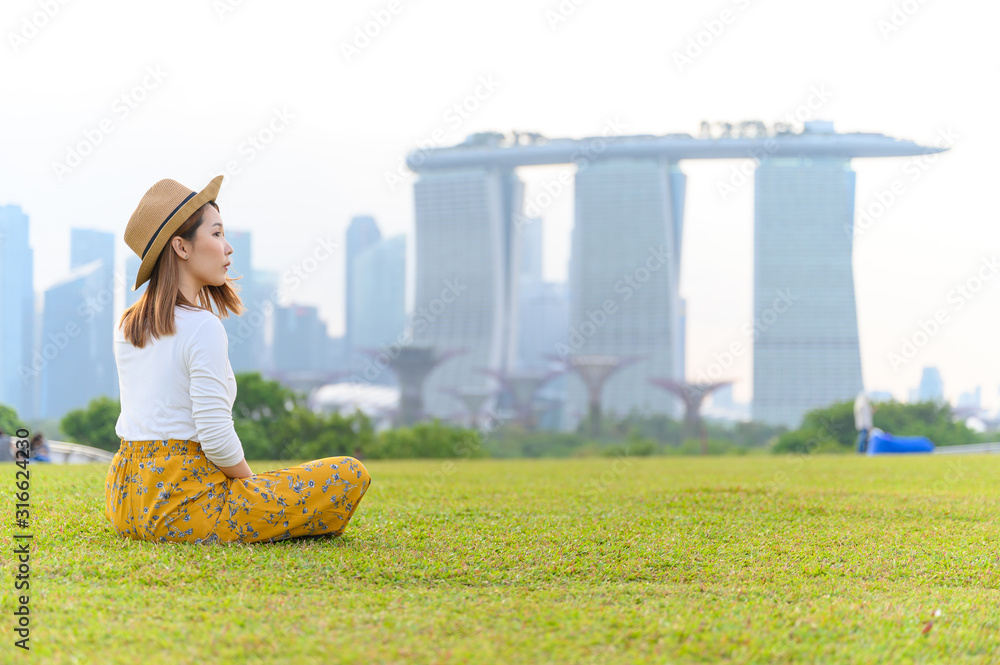 新加坡度假时，一名年轻的亚洲女子坐在滨海公园，背景是滨海湾