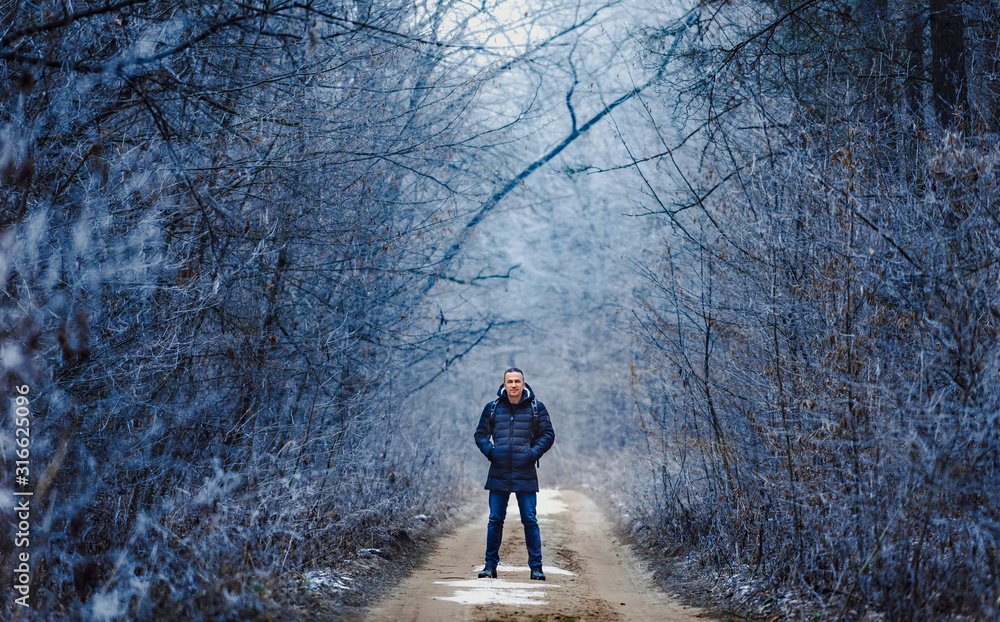 Handsome man in winter cloth standing in park and looking at camera. Snow covered trees. Park in win