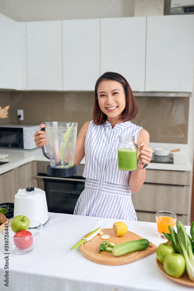 美丽的亚洲女人在厨房里用搅拌机倒奶昔