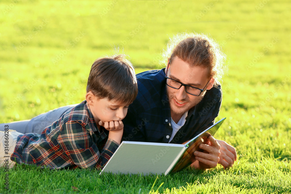 Father and his little son reading book outdoors