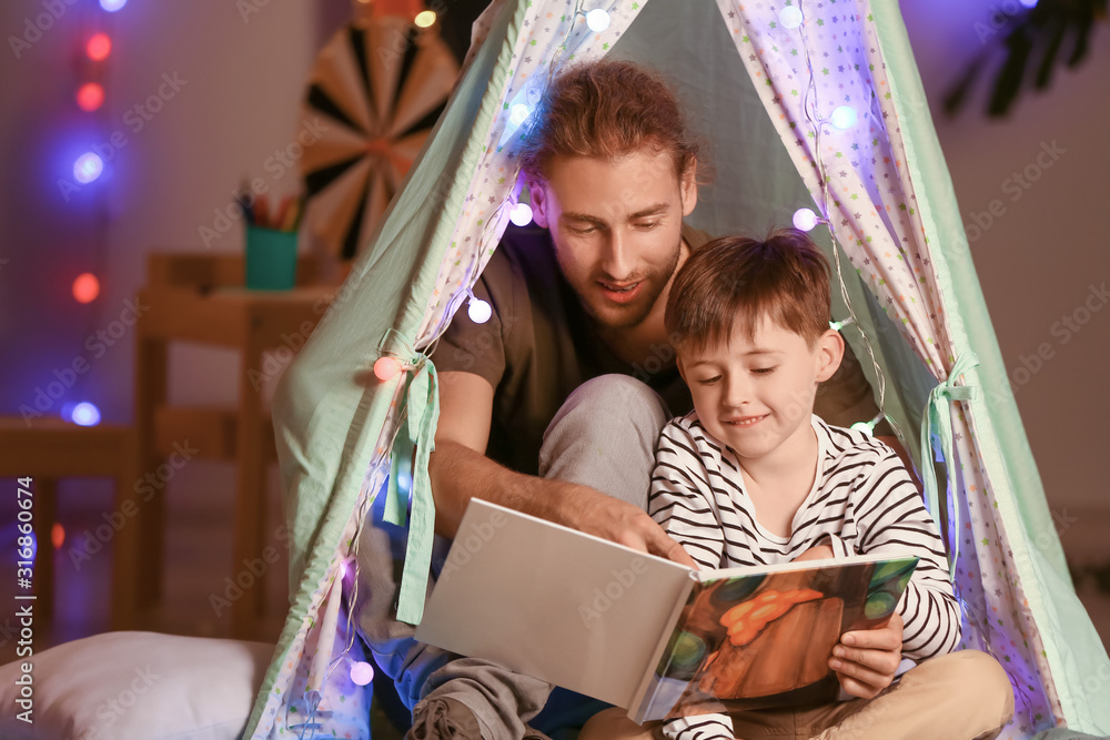 Father and his little son reading book in evening at home