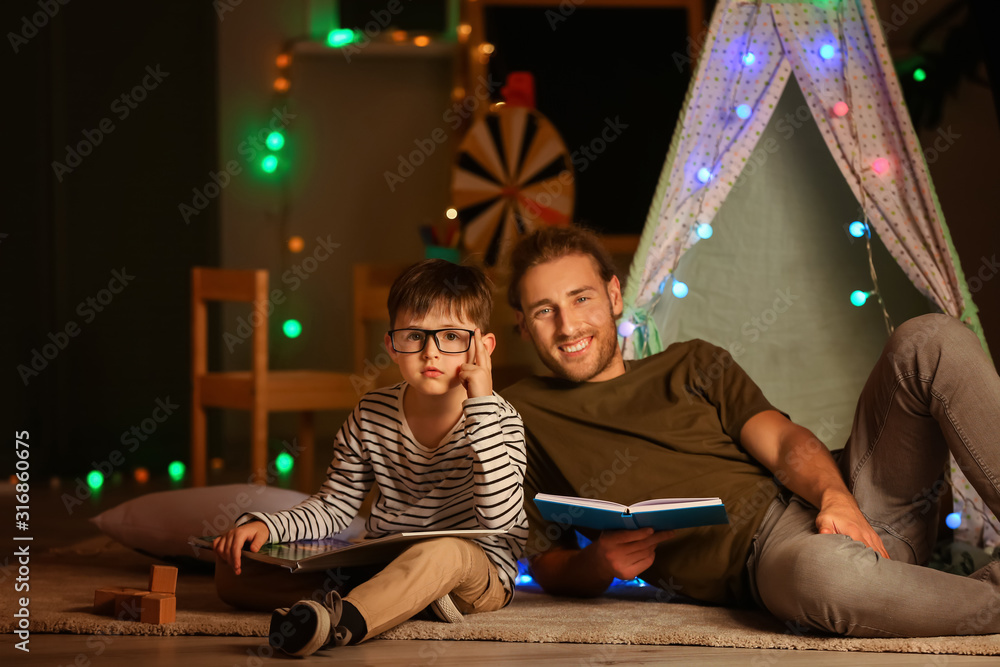 Father and his little son reading books at home in evening