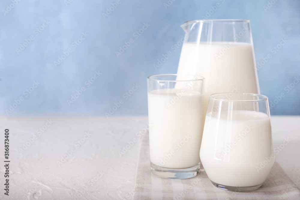 Glasses and jug of tasty milk on white table