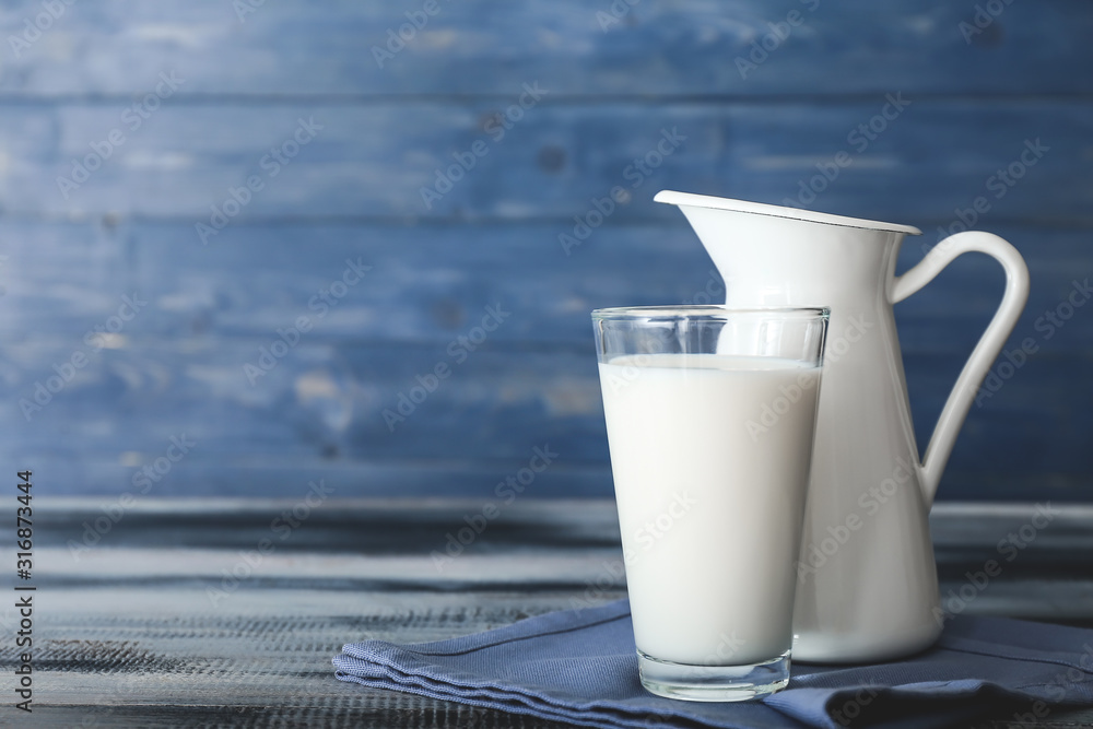 Glass and jug of tasty milk on wooden table