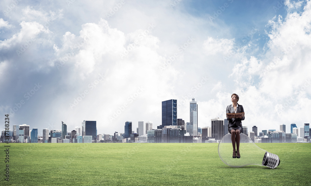 Woman with open book sitting on big light bulb