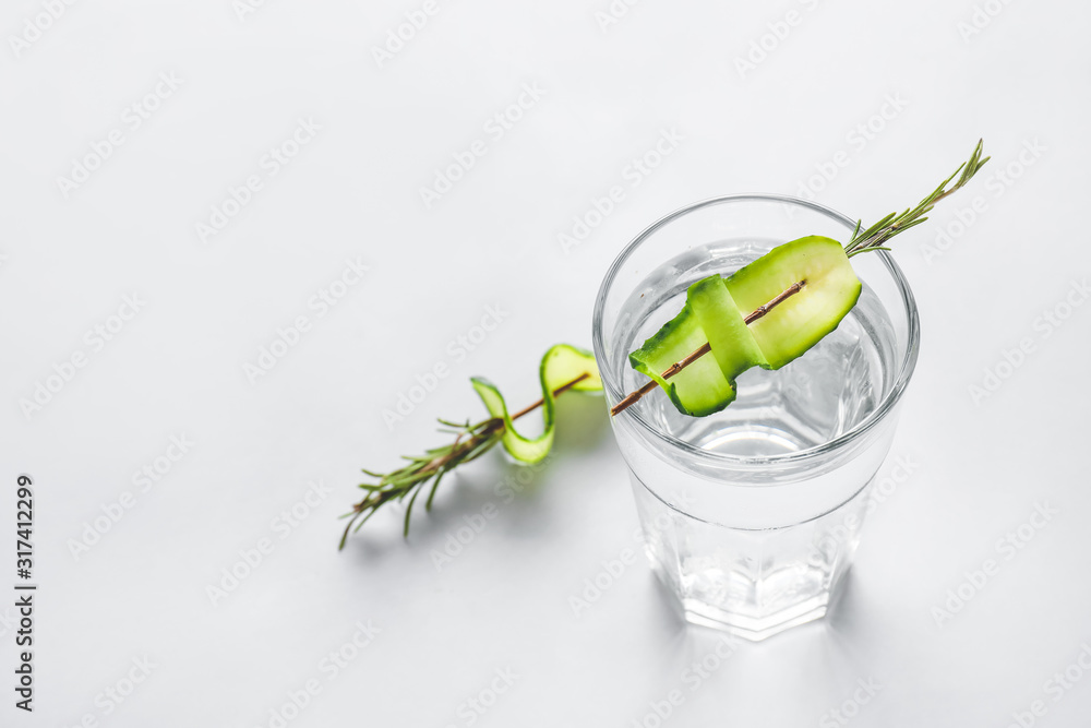 Glass of cold cucumber water on light background