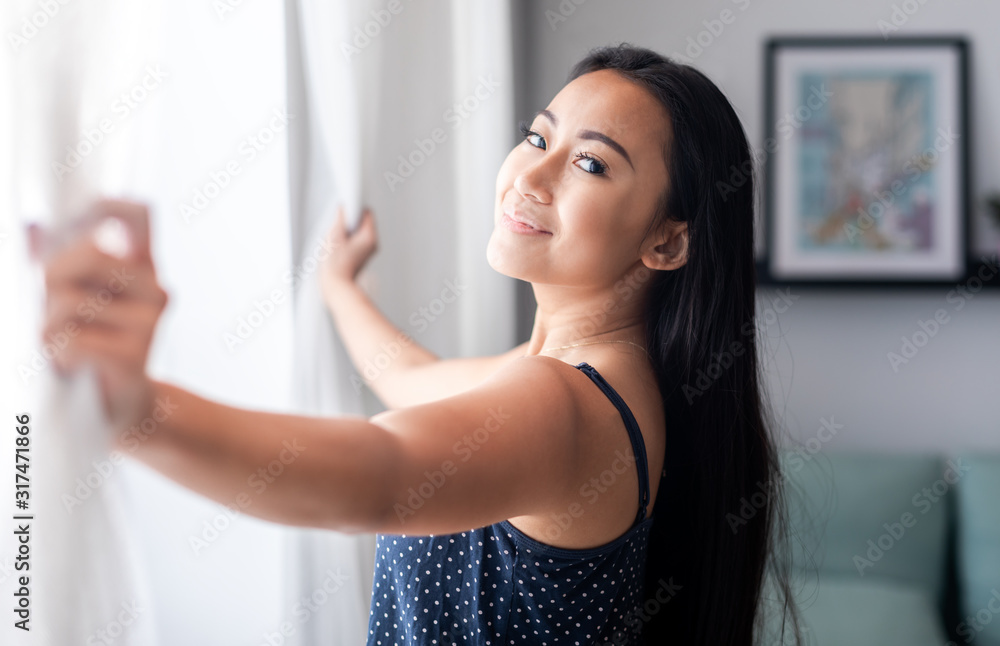 亚洲女人在家里的窗户上打开蕾丝窗帘