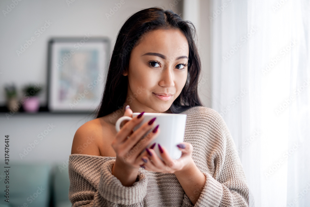 悠闲的亚洲女性在家里喝杯茶或咖啡度过休闲时光