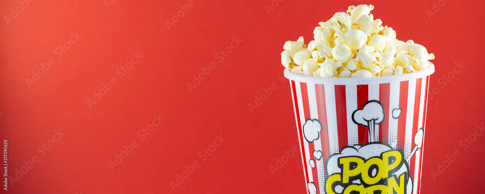 Butter popcorn in a red popcorn cup, snack in the house or cinema on a red background