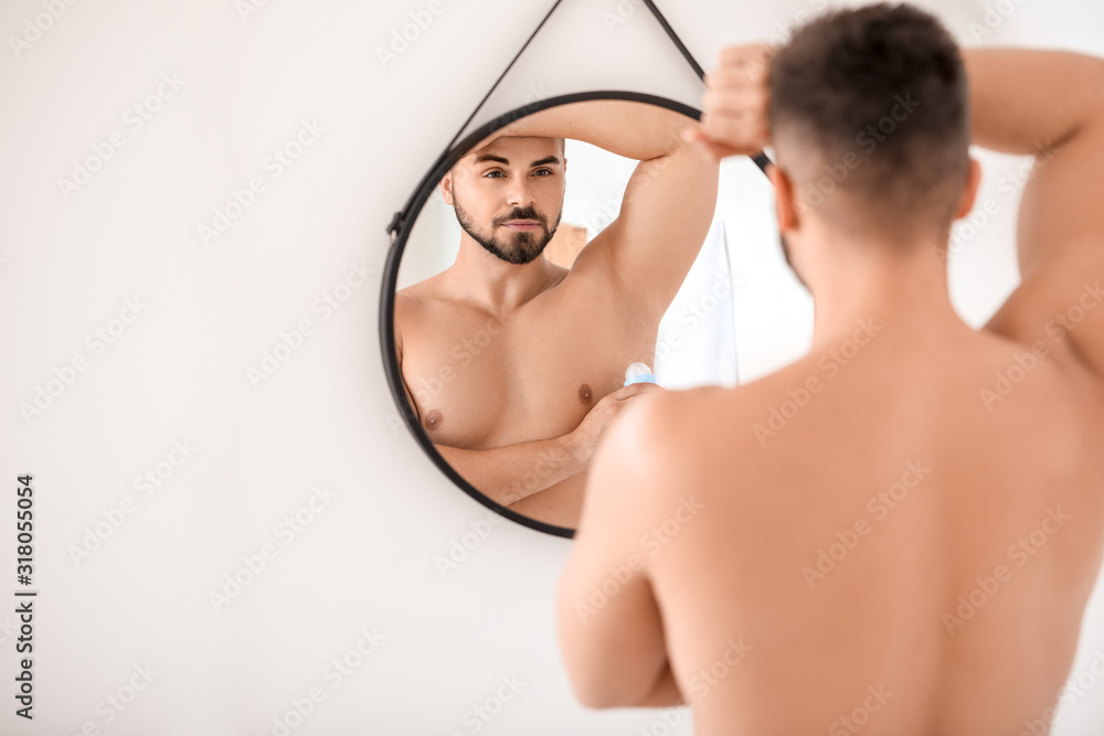 Handsome young man using deodorant in bathroom