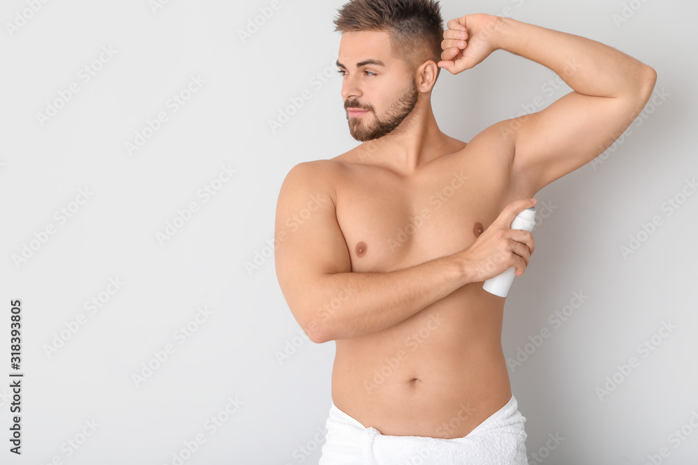 Handsome young man using deodorant on light background