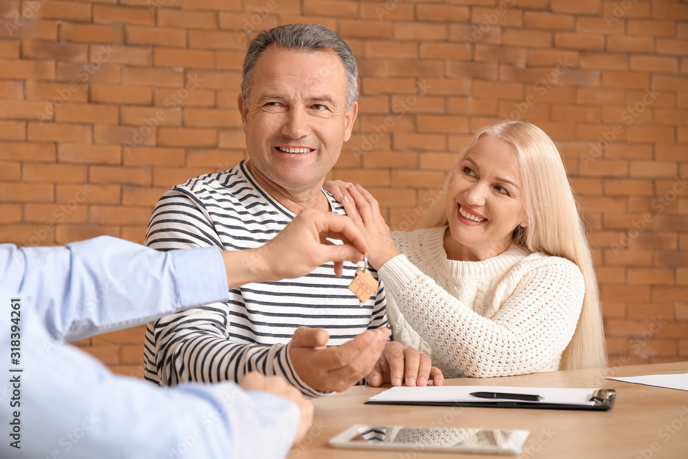 Real estate agent giving a key from new house to mature couple