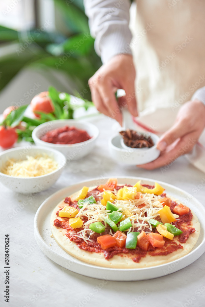 Bakers hand placing ingredients on pizza