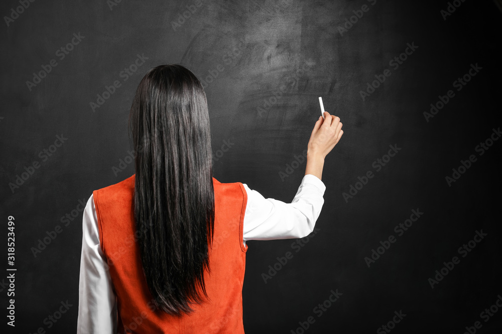 Female teacher writing on blackboard in classroom