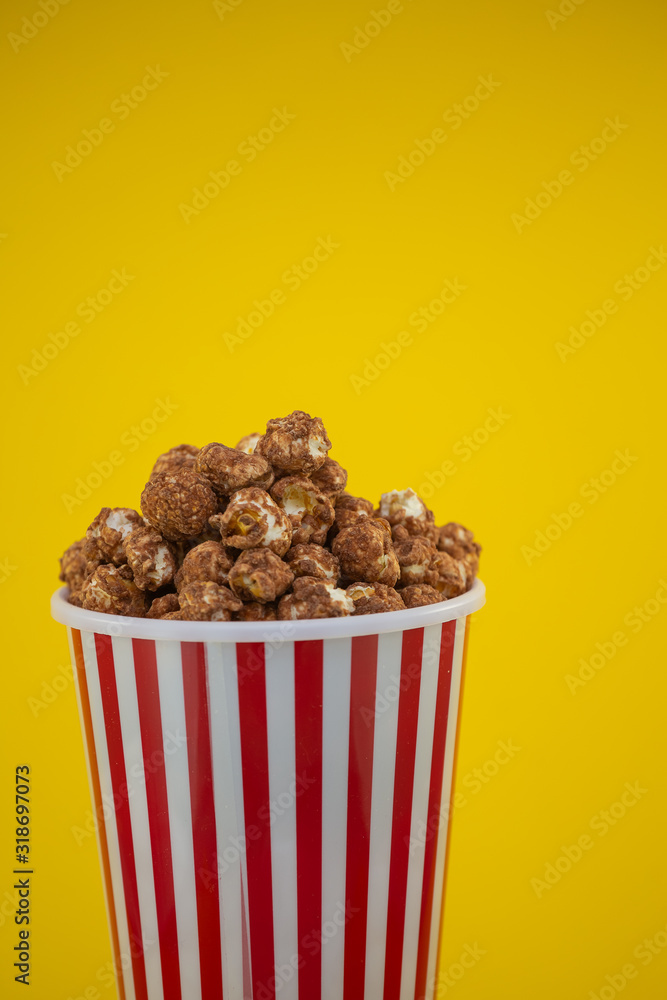 Butter popcorn in a red popcorn cup, snack in the house or cinema on a yellow background