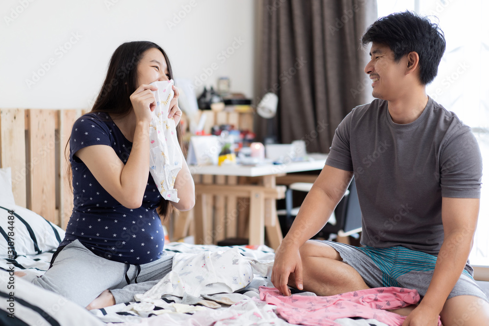 亚洲情侣，她怀孕了，很开心，他们正在为孩子挑选衣服。