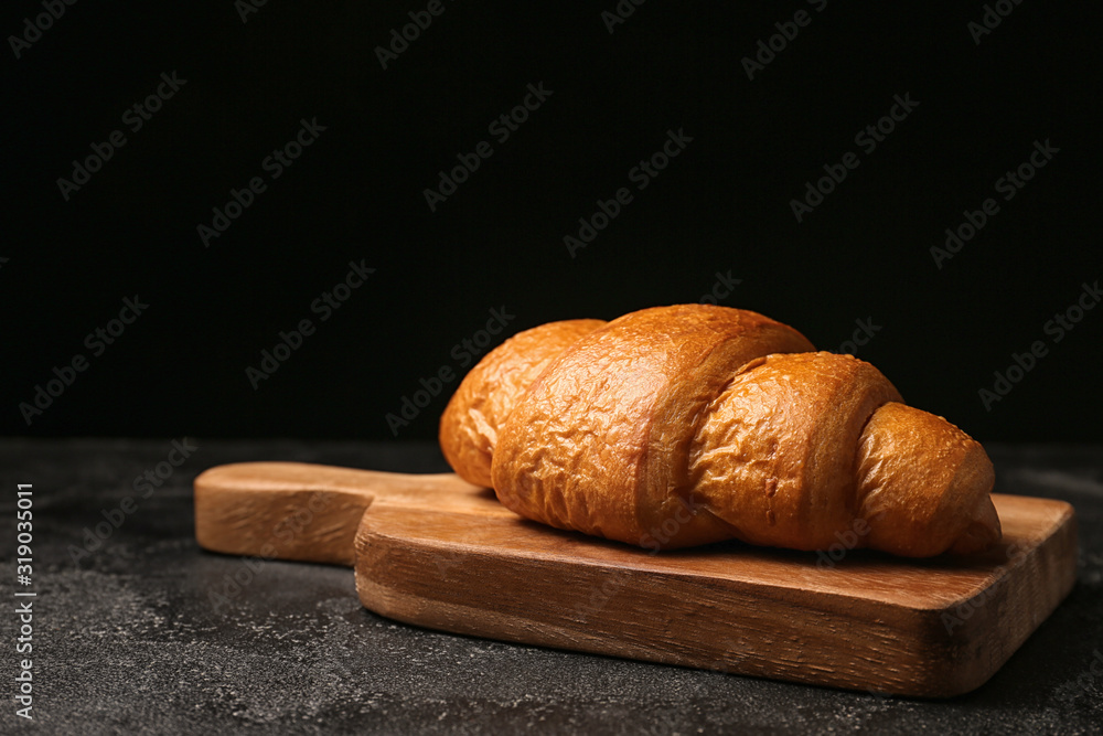 Board with tasty croissant on dark background