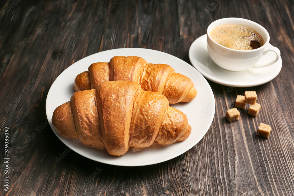 Plate with tasty croissants and cup of coffee on table