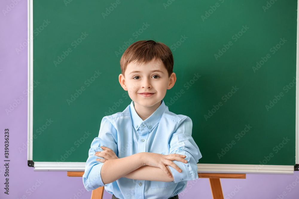 Little schoolboy near blackboard on color background