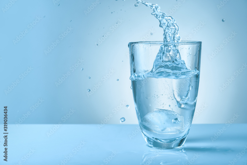 Glass of fresh water with splash on color background