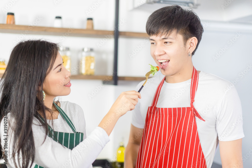 可爱的情侣在厨房里穿着围裙。烹饪蔬菜沙拉。素食情侣展示新菜单