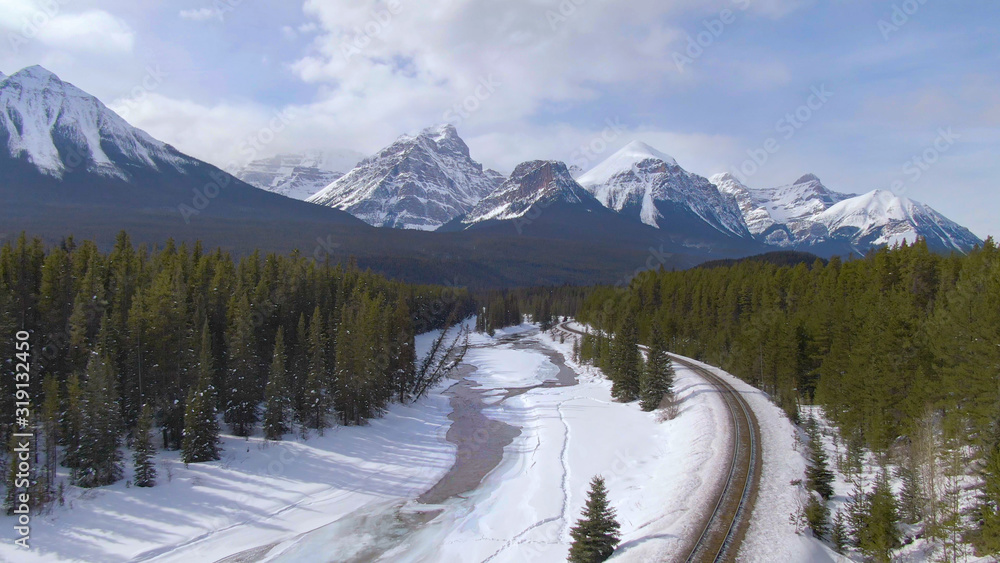 AERIAL: Flying above a frozen river and toward the spectacular mountain range.