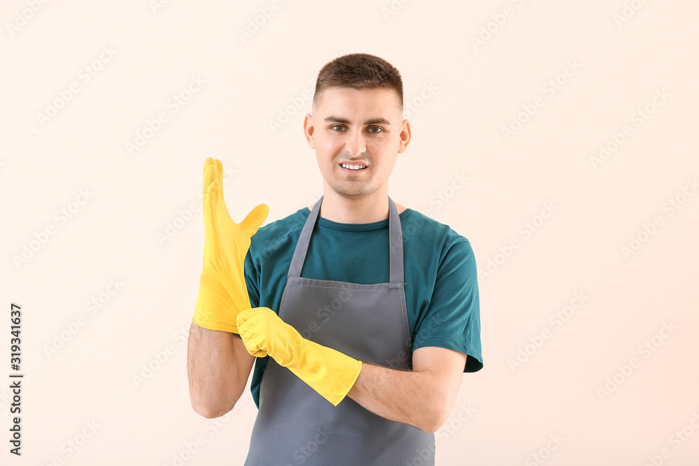 Portrait of janitor putting on rubber gloves against light background