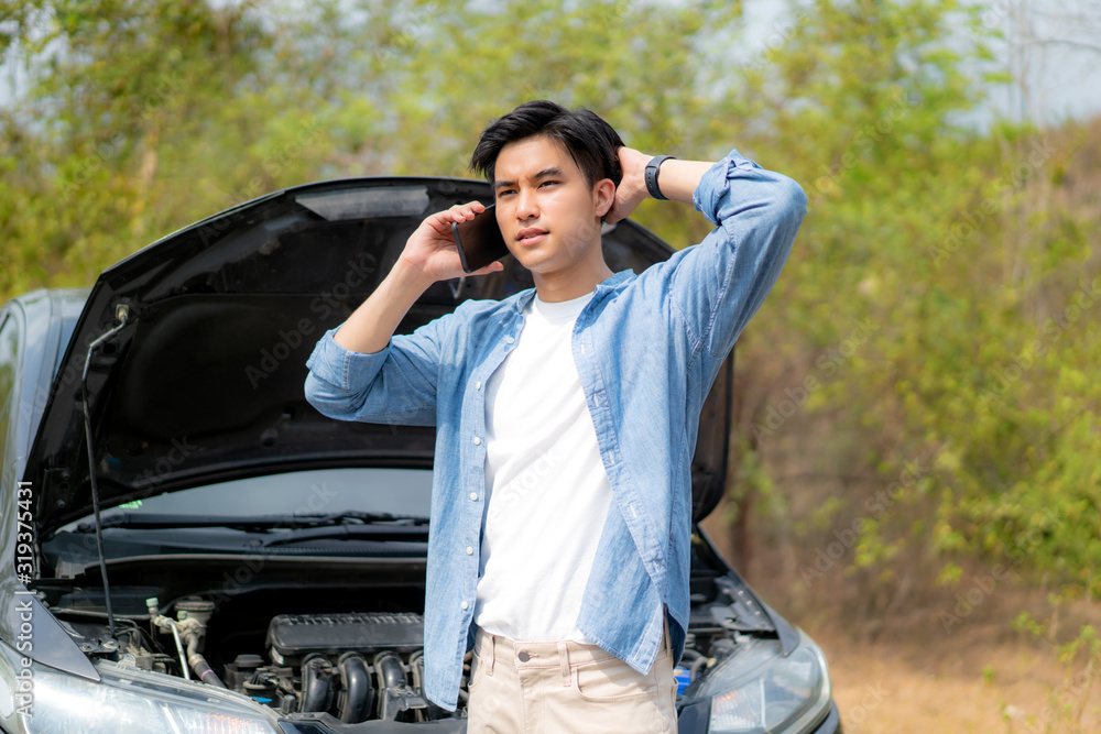 Asian young unhappy man talking on a cell phone  in front of the open hood  broken down car On Count