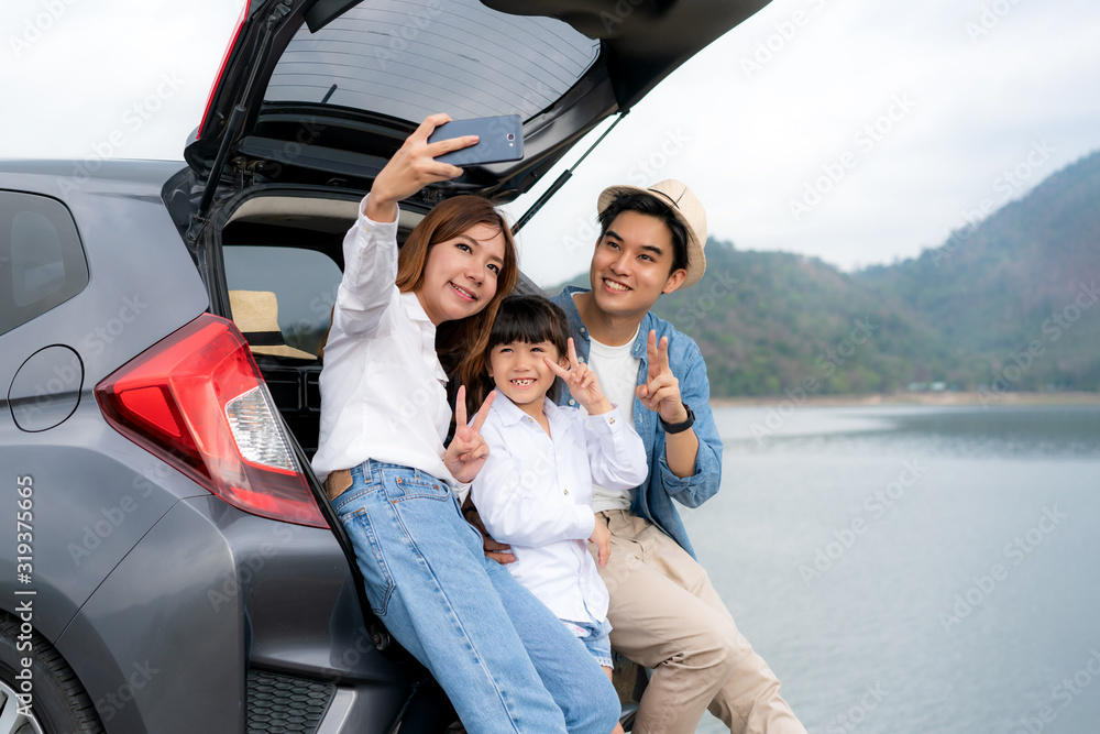 Portrait of Asian family sitting in car with father, mother and daughter selfie with lake and mounta