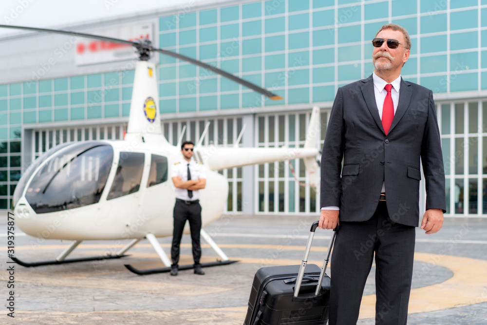 Elderly Businessman manager with Luggage walking from helicopter when he arrive destination at helip