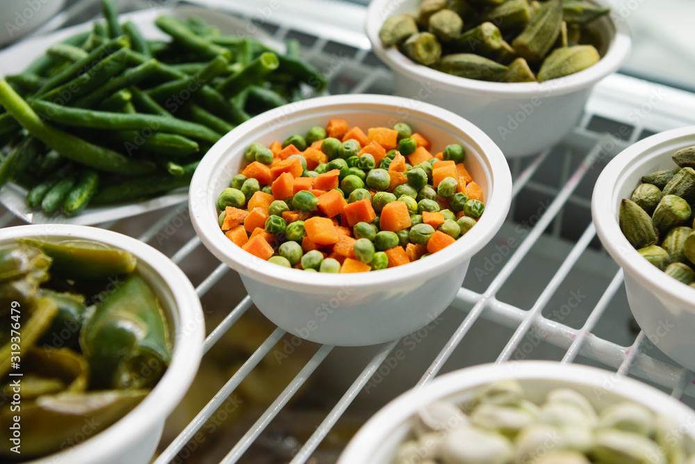 A frozen mixture of carrots and green peas lies on a white plate. Next to the plates are other froze