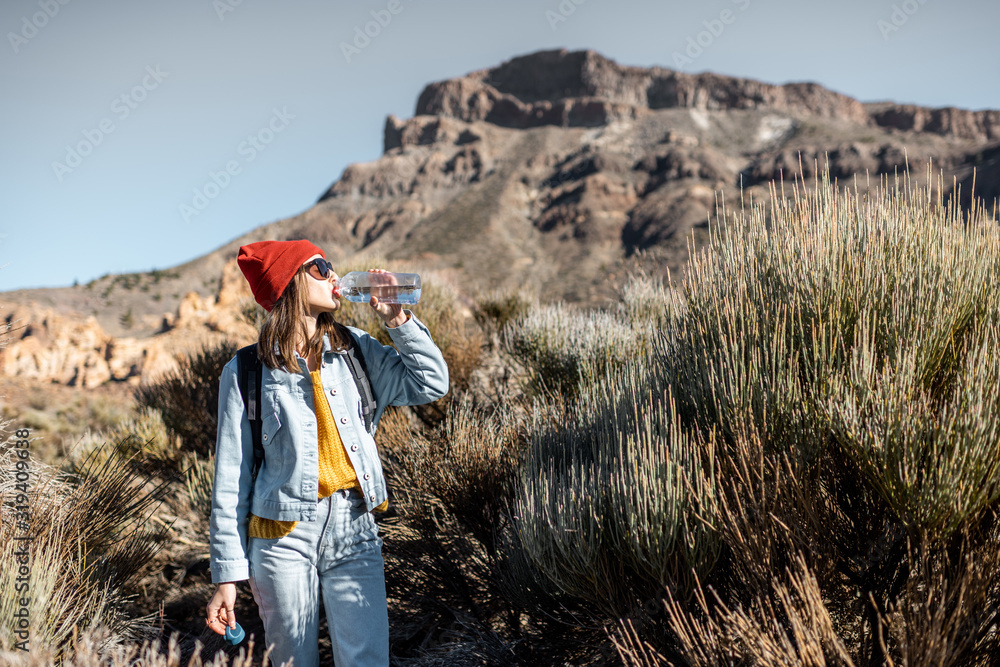 Young woman in red hat traveling with backpack on the volcano valley, feeling thirst and drinking wa