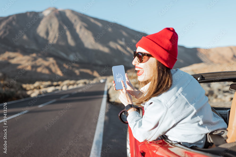 快乐的女人在火山谷开车旅行，靠在车窗外，手里拿着smartpho