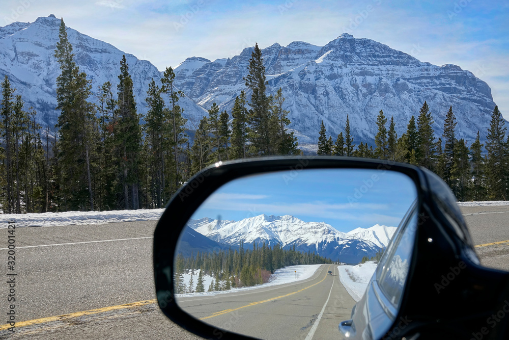 CLOSE UP: Side mirror view of Icefields Parkway route and snowy mountains.