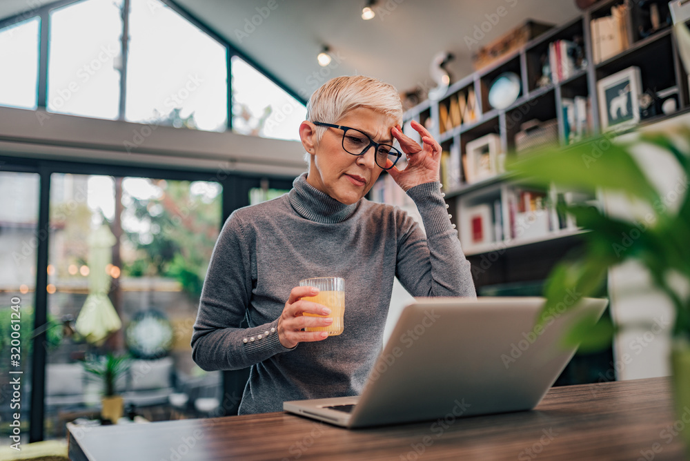 Mature woman having a headache while sitting in front of laptop at home, portrait.