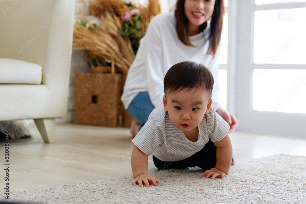 亚洲婴儿下定决心爬行。母亲自豪地看着孩子的成长。她的脸是