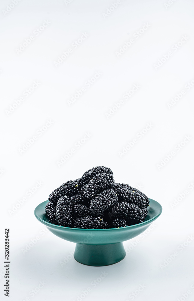 Dark green tall plate filled with fresh mulberries on white background