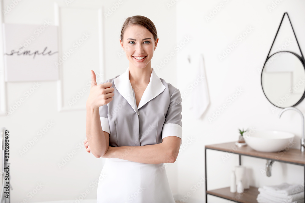 Beautiful chambermaid showing thumb-up in hotel bathroom