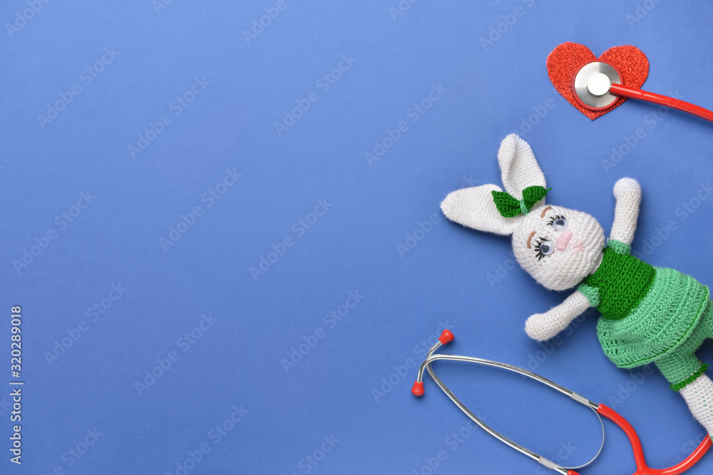 Stethoscope, heart and baby toy on color background