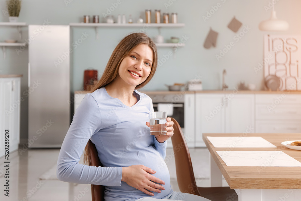 Beautiful pregnant woman with glass of water in kitchen