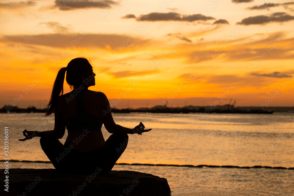 Silhouette of woman sitting on the rock  doing yoga with sunset background