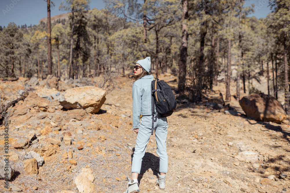 年轻女子穿着休闲，背着背包在火山上高山的森林中行走