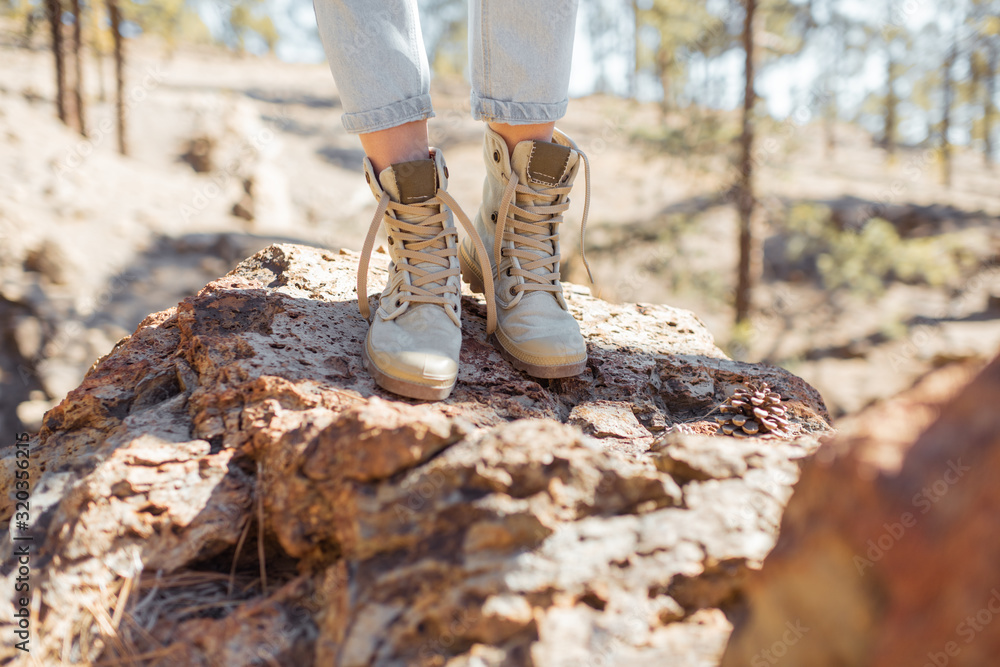 Woman standing on the stones, hiking on a rocky land, close-up on legs in trekking shoes