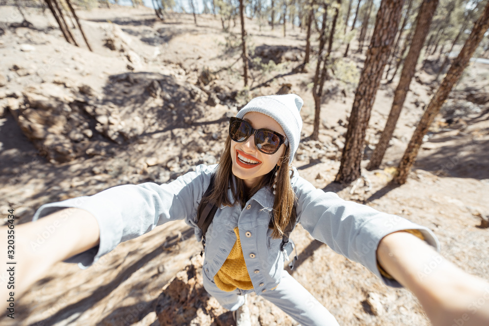 年轻女子在岩石山脉的森林中旅行时自拍