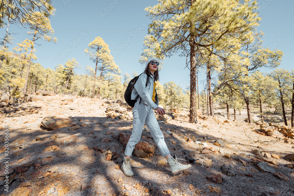 Young woman dressed casually walking with backpack in the forest highly in the mountains on the volc