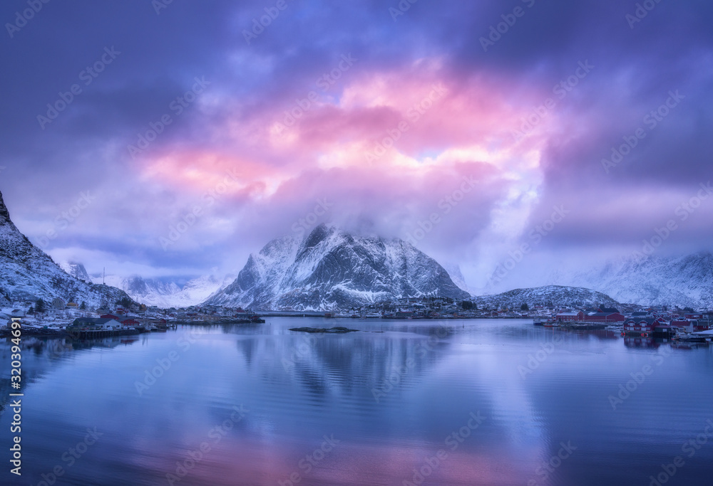 Aerial view of snowy mountain, village on sea coast, purple sky at sunset in winter. Top view of Rei