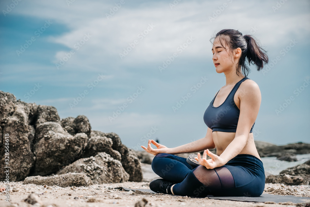 年轻的亚洲女性在安静的岩石码头练习瑜伽，背景是大海。运动和娱乐