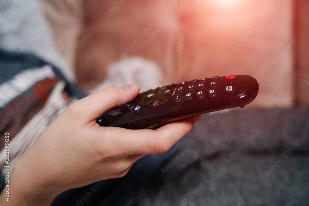 Hand holding tv remote control and surfing programs on television. Teenage boy watching TV in the li