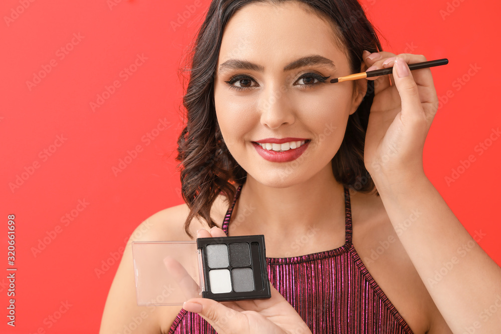 Makeup artist working with beautiful young woman on color background